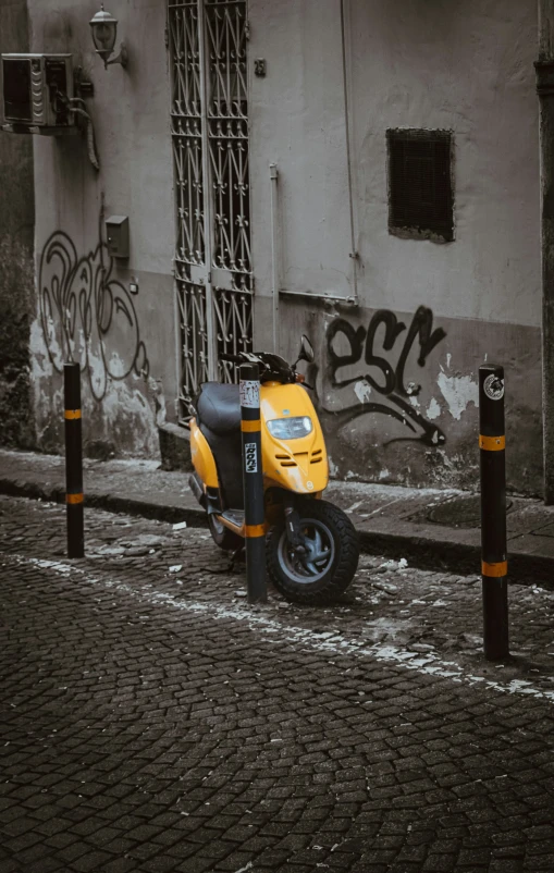 a yellow scooter parked by a wall with graffiti on it