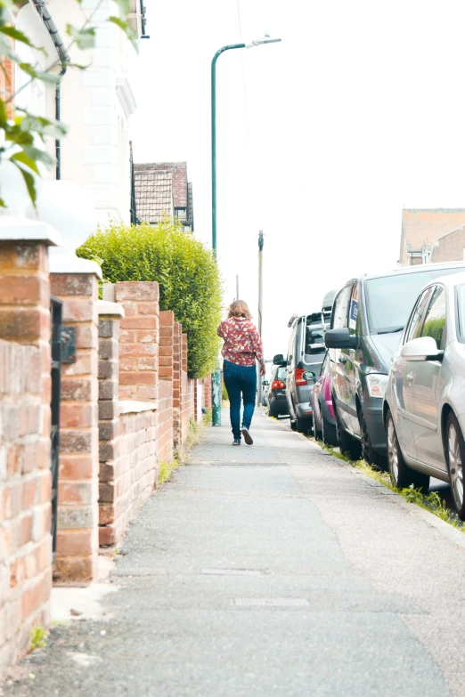 a woman walking down the street with two cars parked beside her