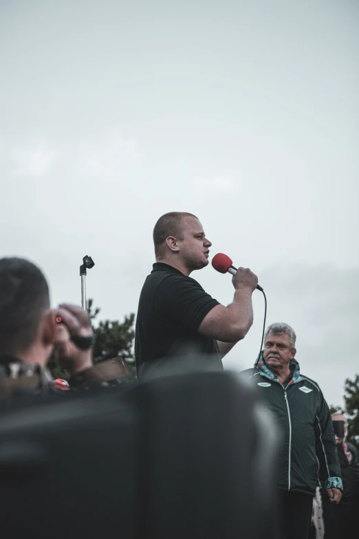 a man speaking into a microphone with people watching