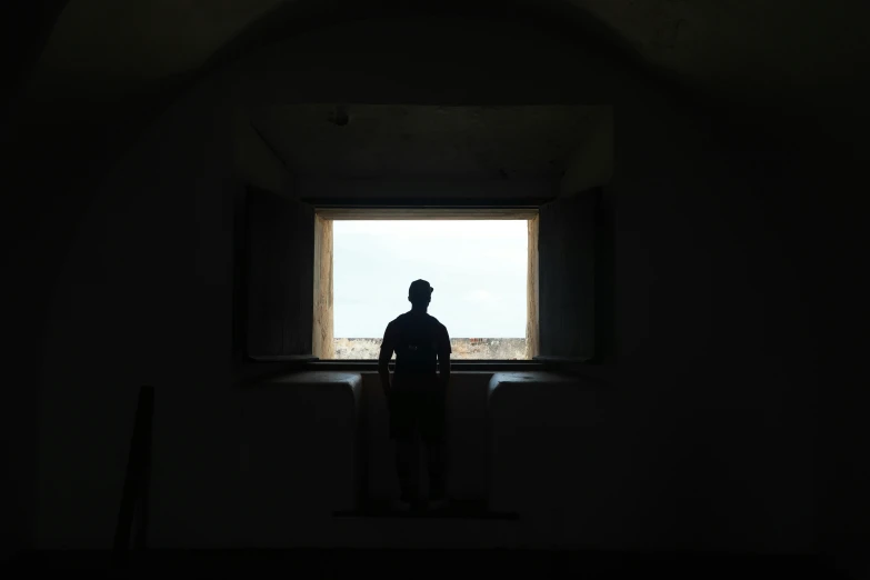 man looking out window in small darkened room