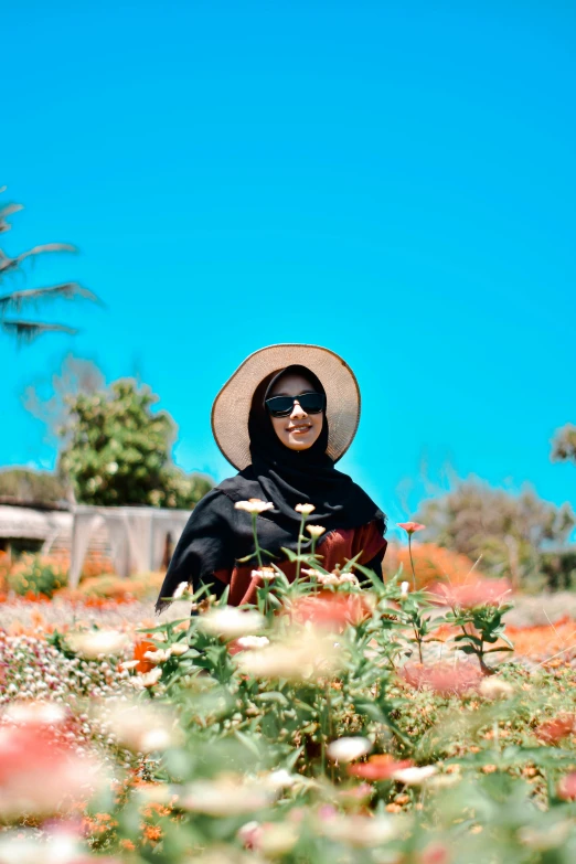 a woman with sunglasses sitting in a field with flowers