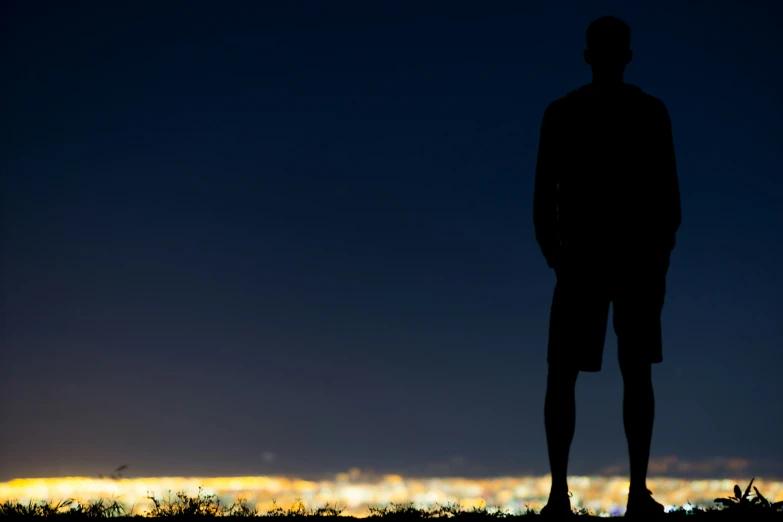 the silhouette of a man in shorts is in front of a night city