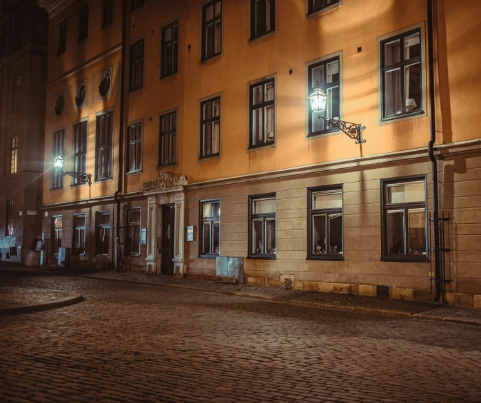 an empty street at night with some lights on and a large building