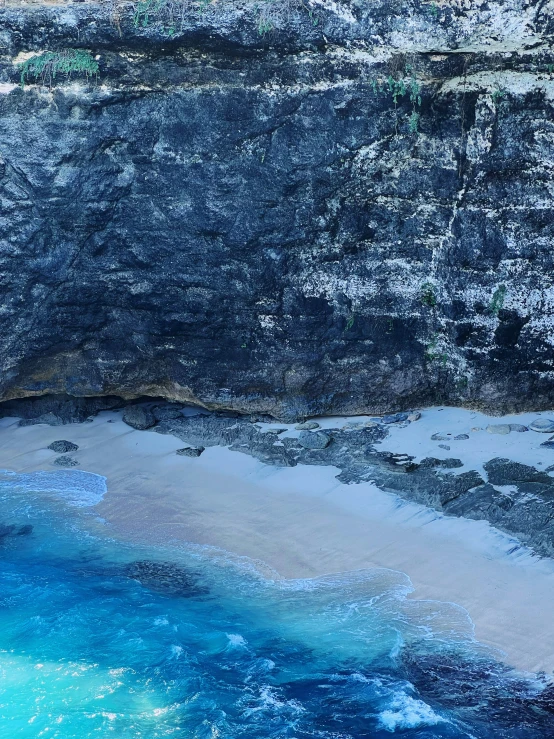 the water is blue in color as it sits next to a large cliff