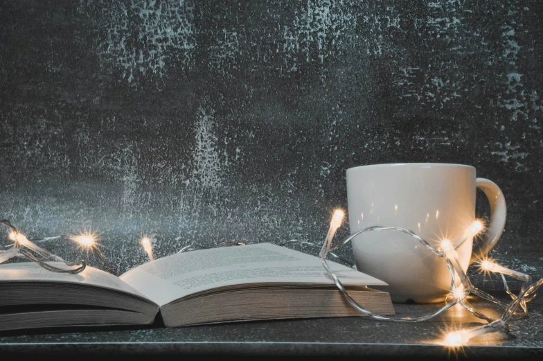 an open book and a cup of coffee with light string