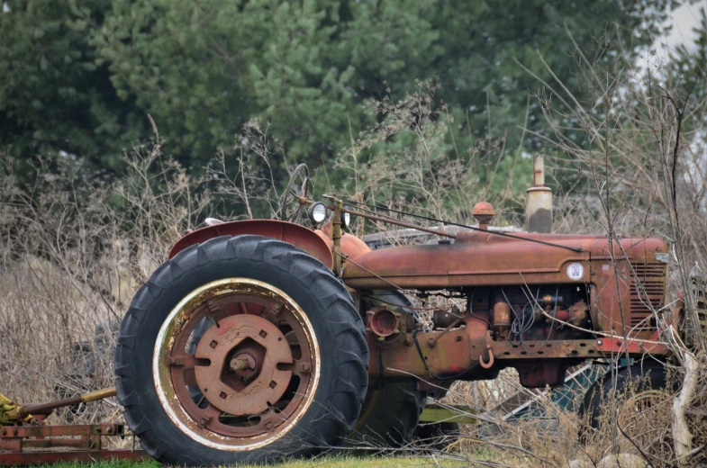 an old rusty tractor in a field with trees in the background