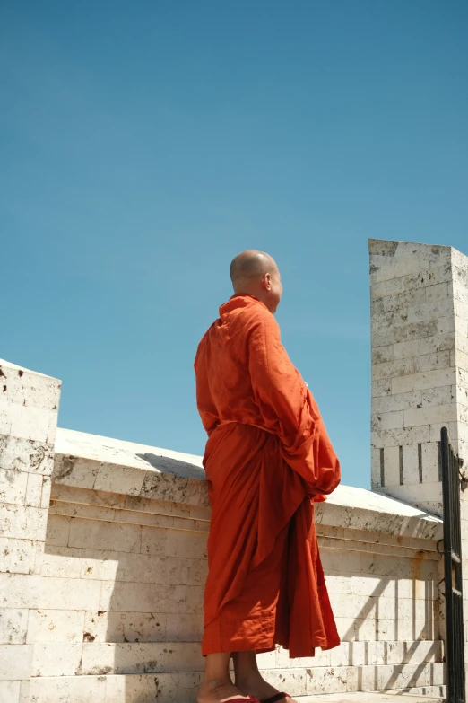 a monk stands on a ledge looking at the sky