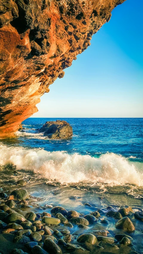 a rocky beach with blue sky and waves coming in