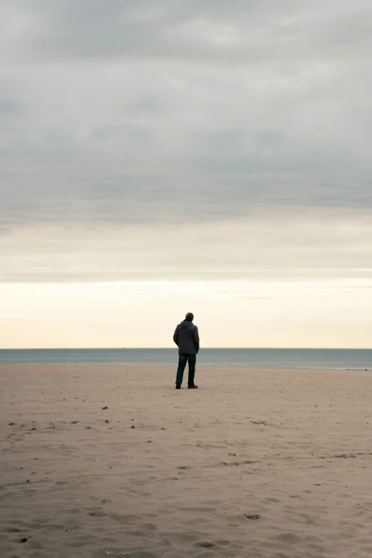 a man walking across a sandy beach towards the ocean