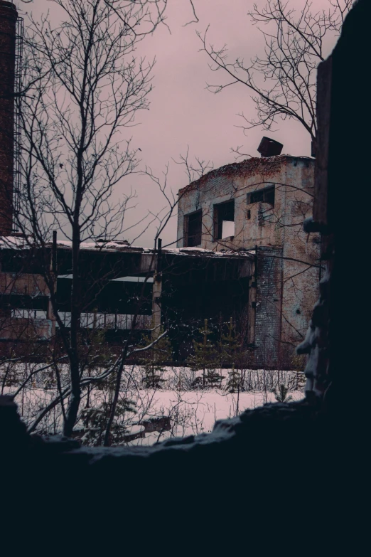 an abandoned building with broken windows is seen through a snowy landscape