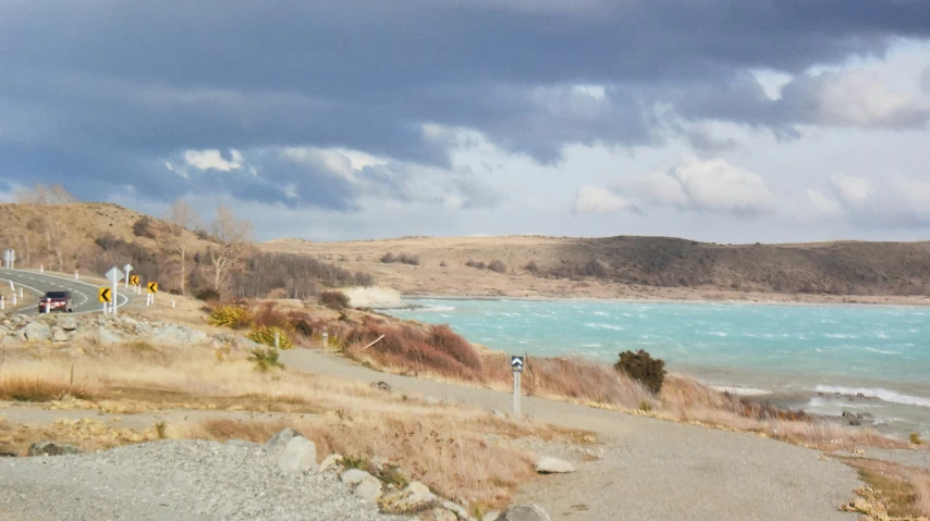 an empty sandy road near a lake on a cloudy day