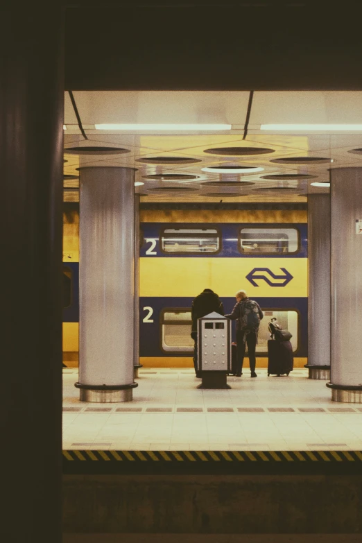 two people stand at a train station in front of an open yellow train