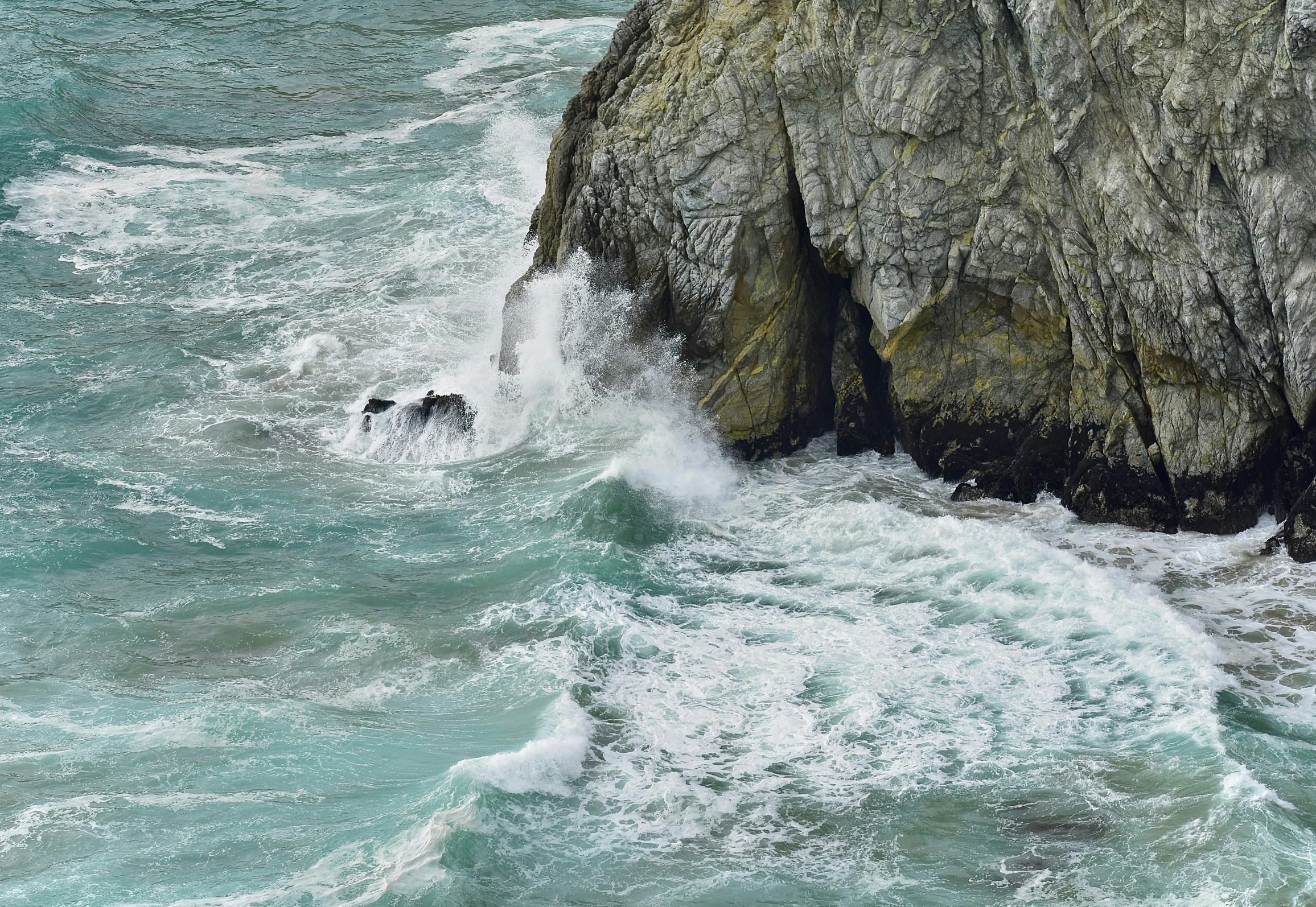 three people stand near some rocks while another swims