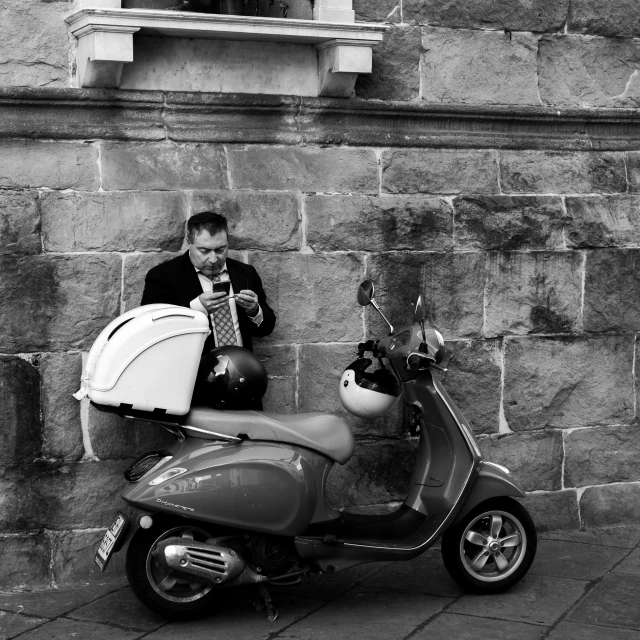 a man sitting on a scooter by a wall and playing on a guitar