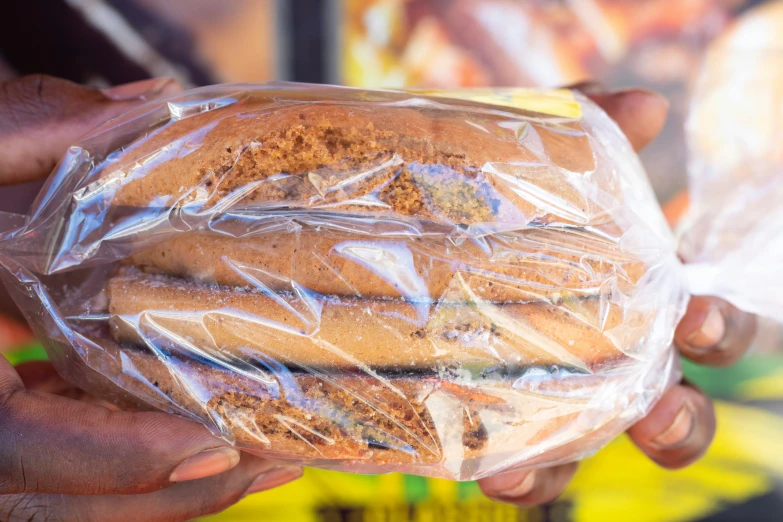 two hands are holding three sandwiches wrapped in plastic