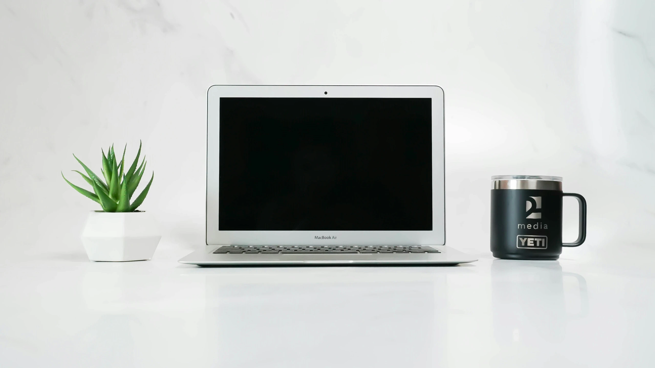 a white desk has a coffee mug on it and a silver laptop