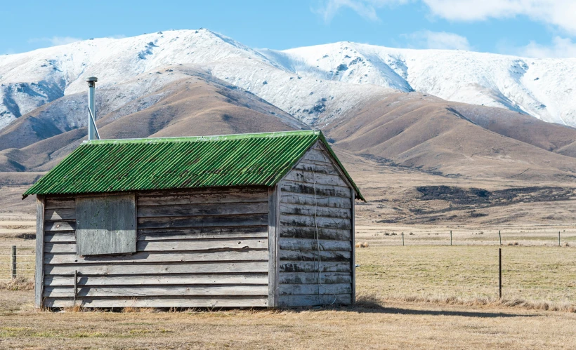 a cabin with a green roof and mountains in the background