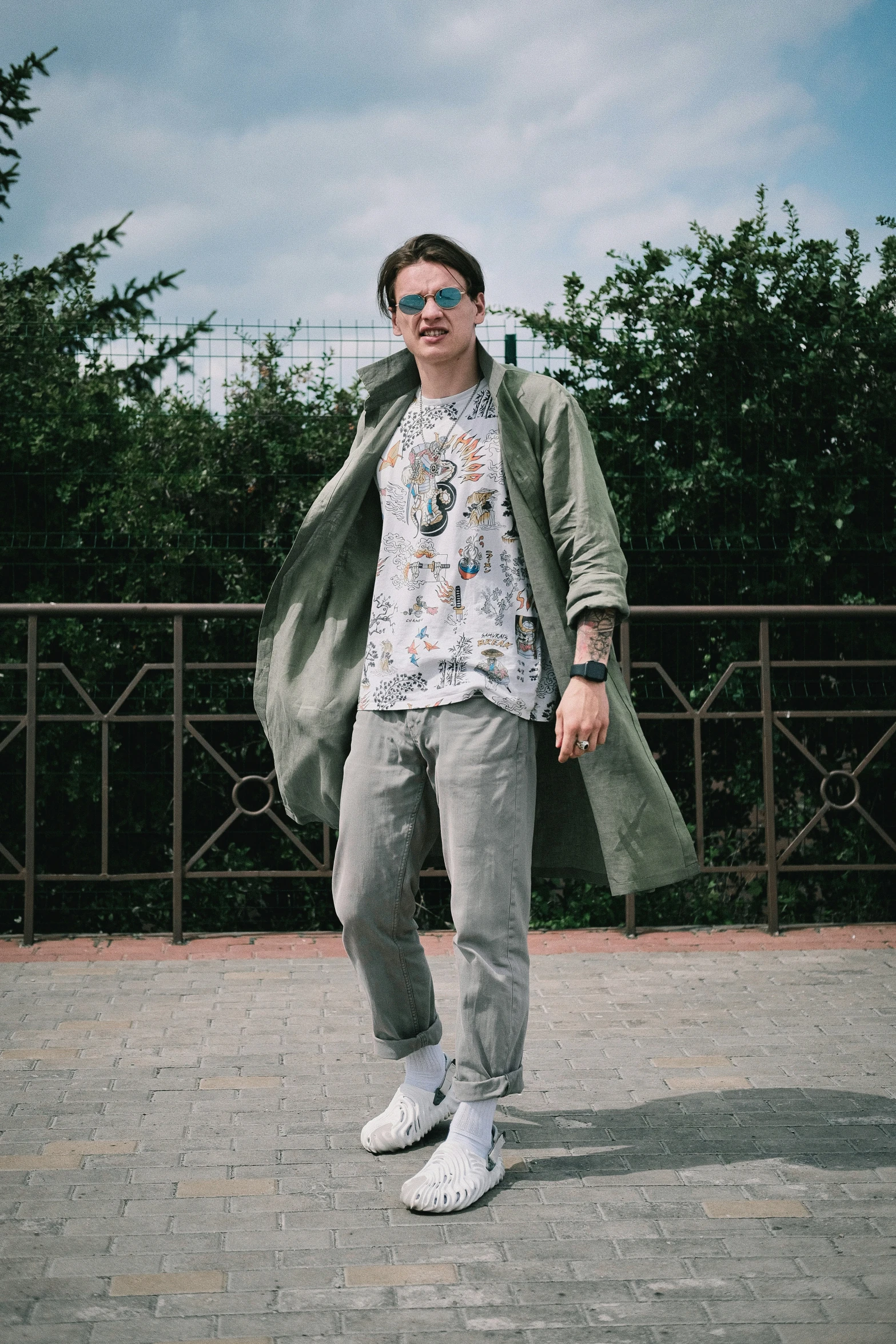 man in sunglasses posing by fence on his skateboard