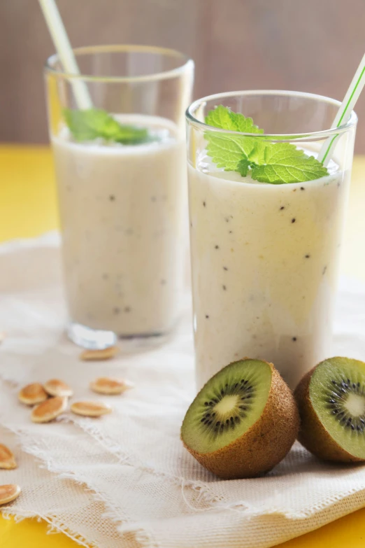 a smoothie, kiwi and nuts are arranged on a white napkin