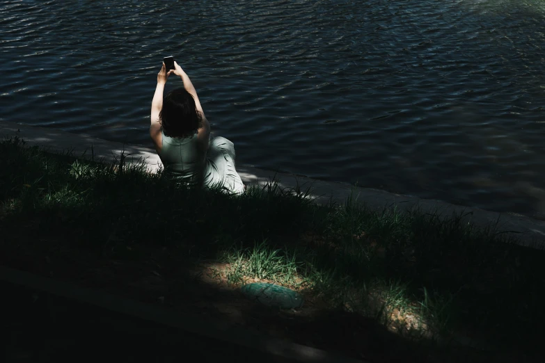 a woman is sitting by the water, with her arms in the air