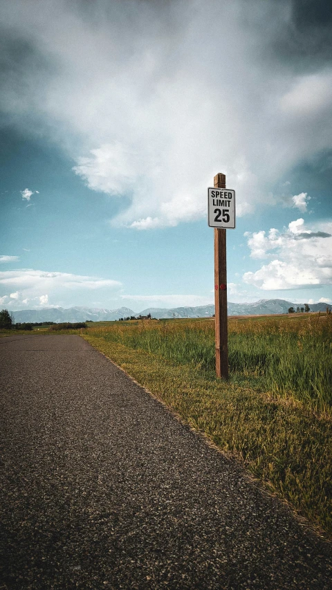 a sign posted next to a paved road under a cloudy sky