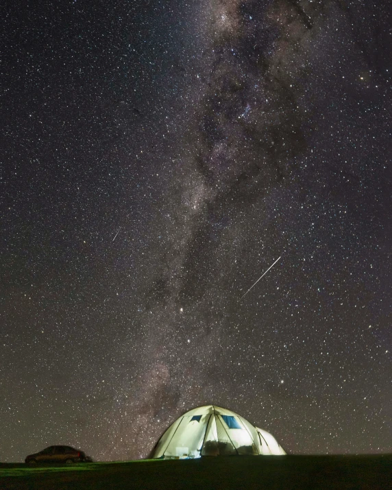 a couple of tents are lit up by the night sky