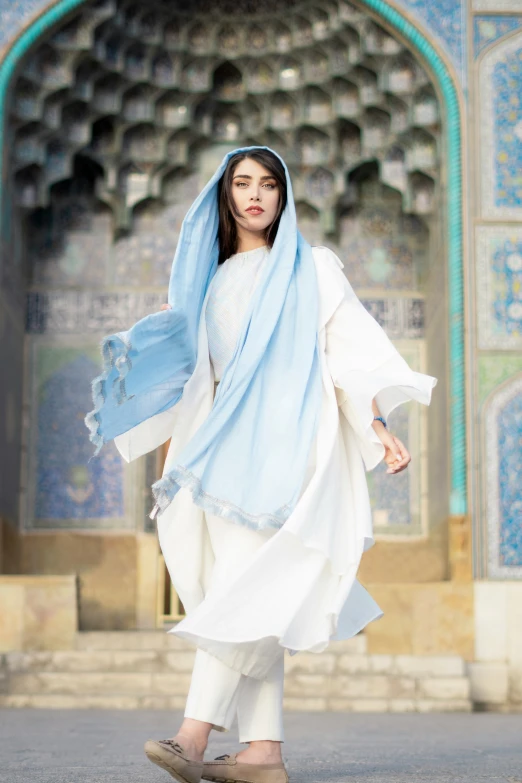 an attractive woman in a white outfit with a blue shawl