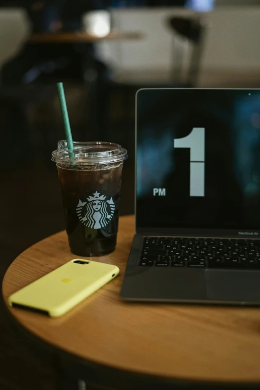 a starbucks coffee on a table with a yellow phone and laptop