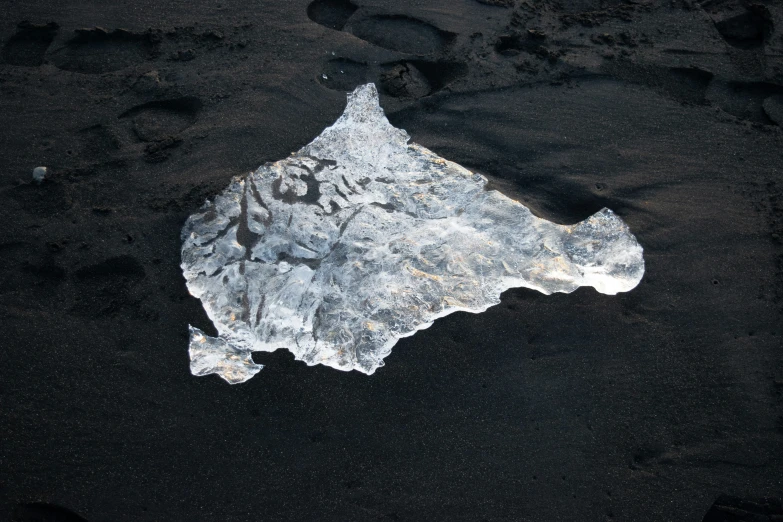 a piece of ice lies in some black sand