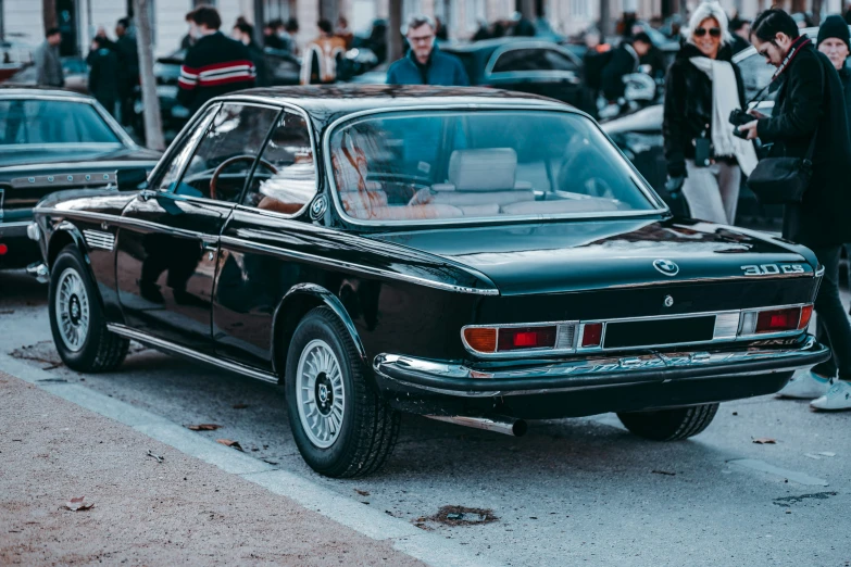 an old black car sits parked on a busy street