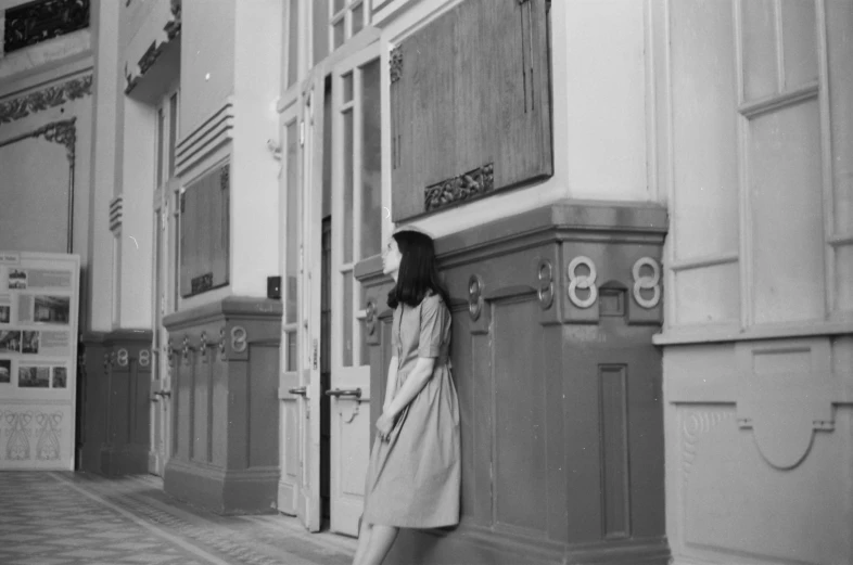 a young woman leans on a closed door, leaning against a wall