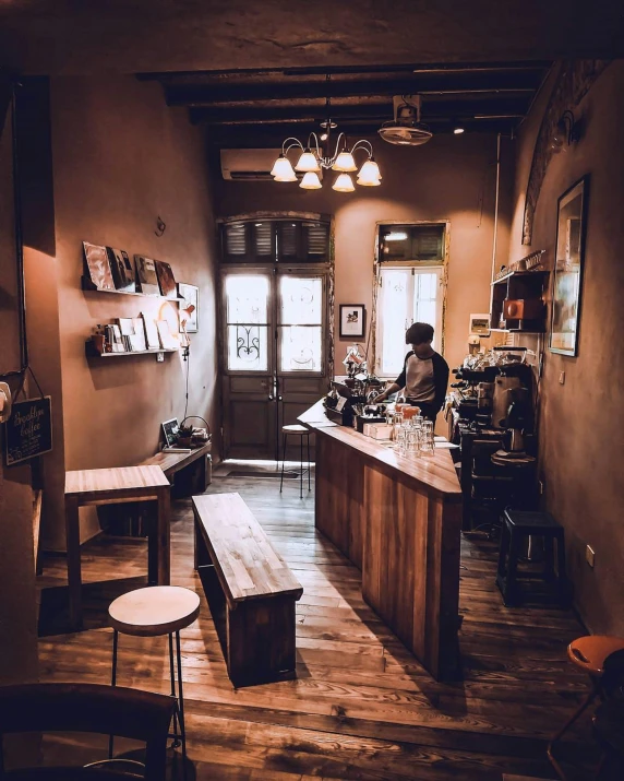 a coffee shop with two wooden benches, a long counter, and a woman standing in front of a coffee machine