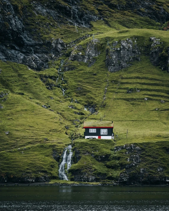 a small house is situated at the base of a waterfall