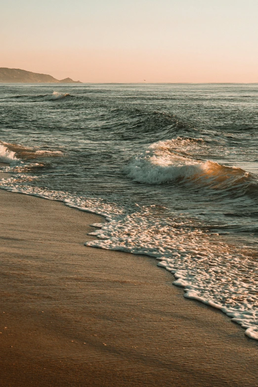 an ocean wave rolls in onto the sandy beach