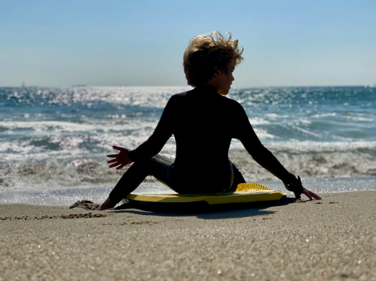 a young person sitting in the sand on a surfboard