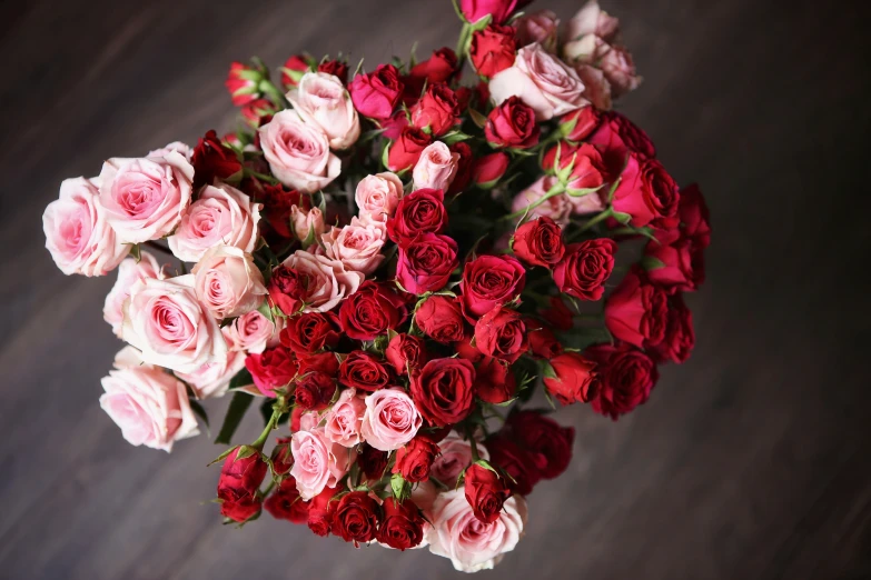 red and pink roses are arranged on a wooden table