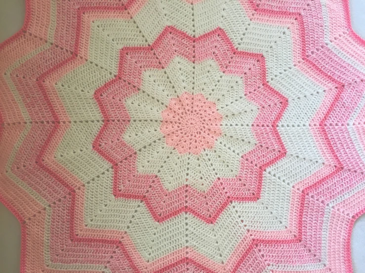 a pink crocheted blanket with an odd looking design on it