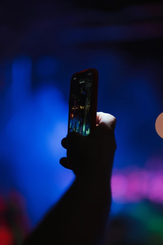 a hand holding up an iphone in front of a brightly lit crowd