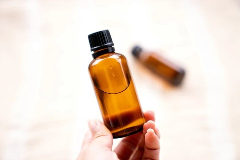 a hand holds an open bottle containing essential oils