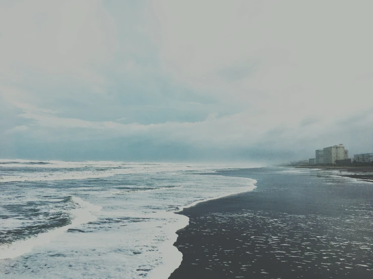 black sand beach on cloudy day with ocean and city skyline