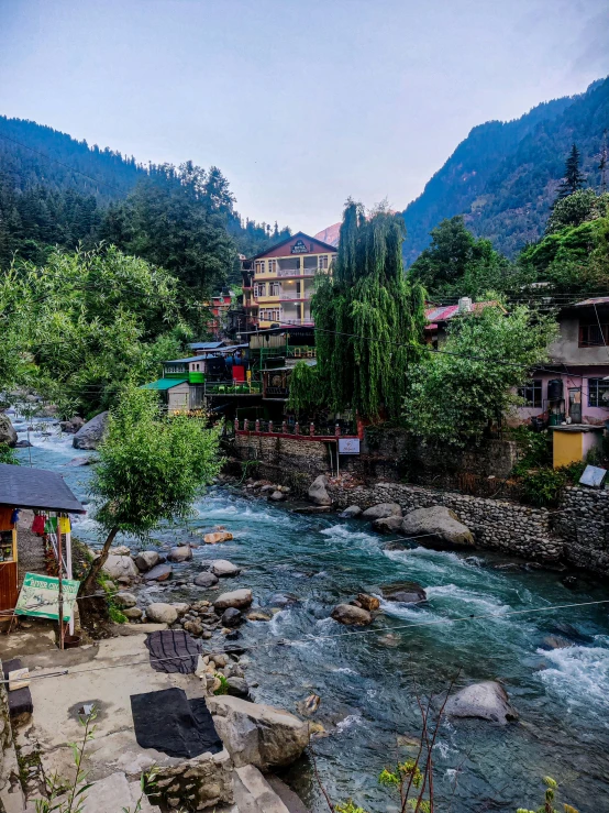 the houses are near a beautiful stream with trees and hills in the background