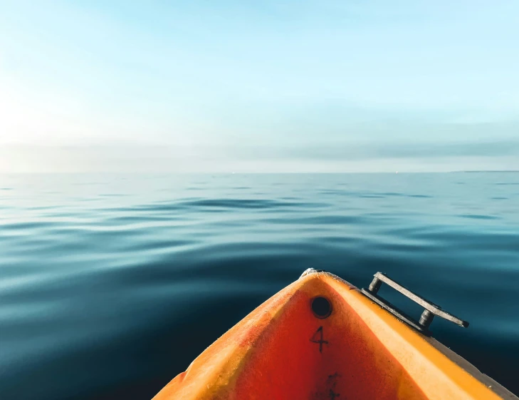 an orange paddle boat floating on the ocean with blue sky in the background