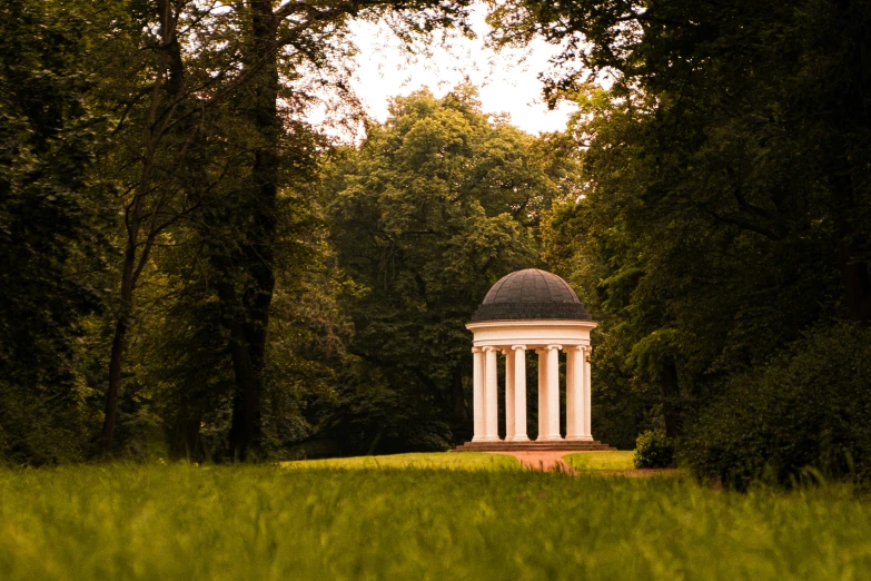 an old white, round monument in the middle of trees and grass