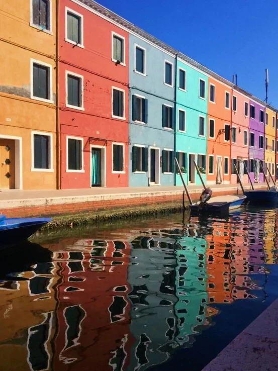 the building that has colorful facades is reflected in the water