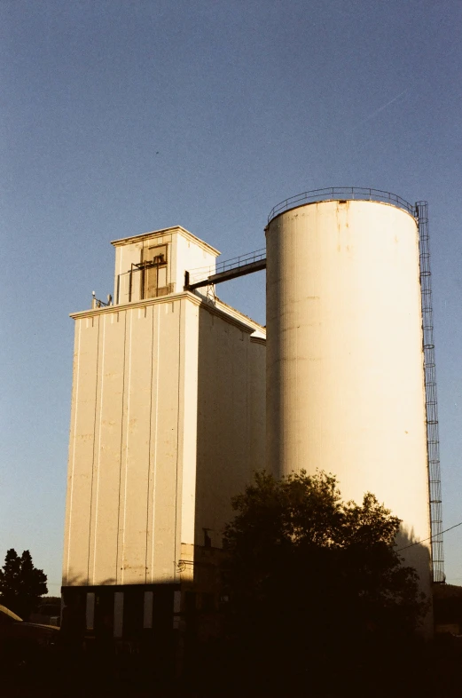 two large white silos are near trees and a blue sky