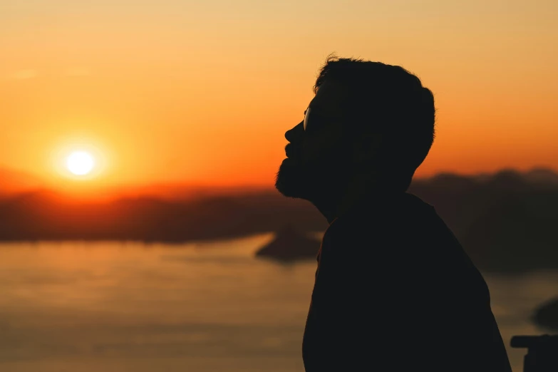 a person standing in front of a body of water with the sun setting