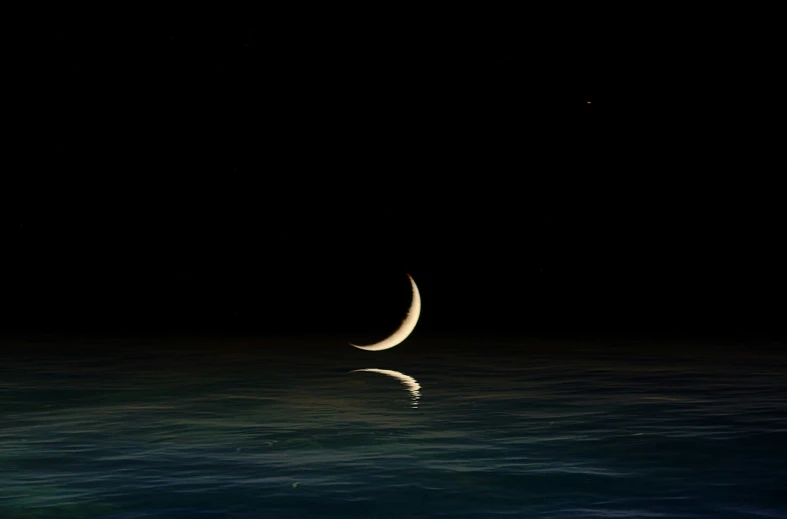 a half moon rises above the ocean at night