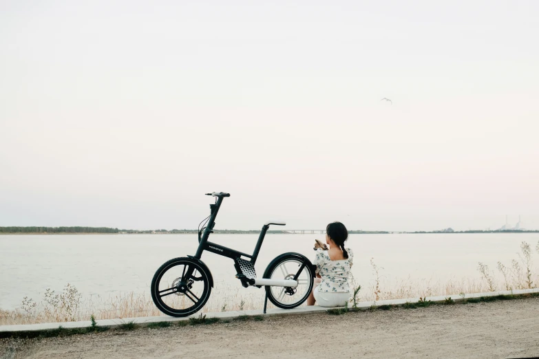 a girl in white dress standing with a bicycle near a water