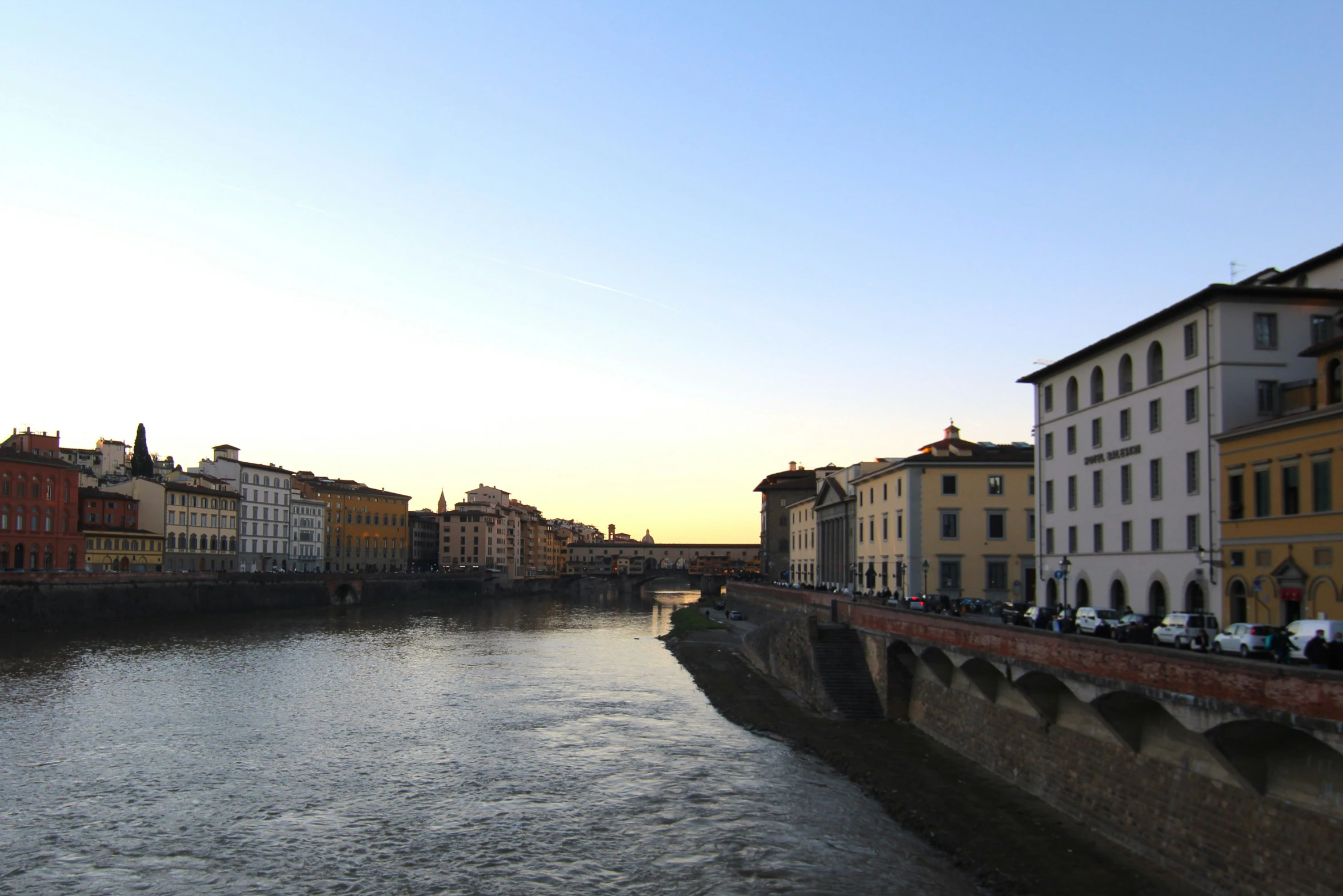 people sitting on the ledges by the water and some buildings