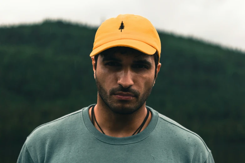 a man wearing a hat standing in front of a mountain